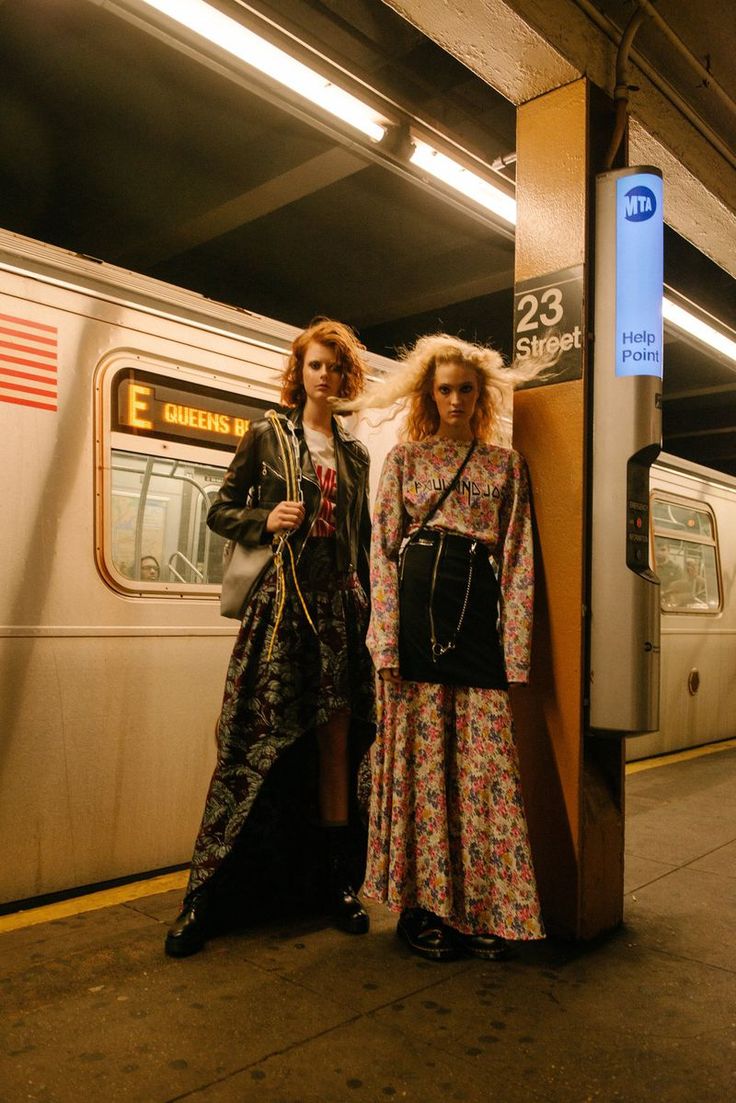 two women standing next to each other in front of a train at a subway station