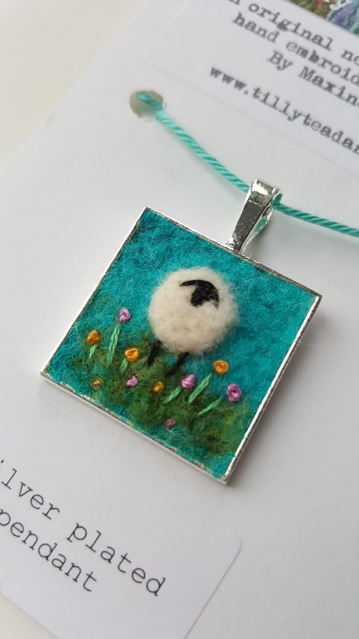 a small square pendant with a white sheep on it's face in the grass