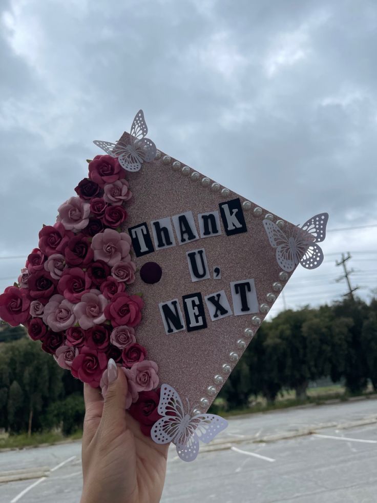 someone holding up a graduation cap that says thank u next with butterflies and flowers on it