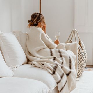 a woman sitting on a couch wrapped in a blanket and holding a glass of wine