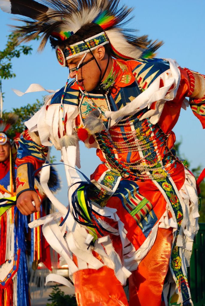 two men dressed in native american clothing and feathered headdress, one is dancing