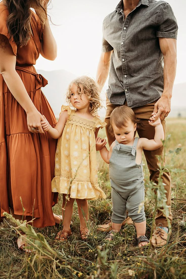 an adult and two children holding hands while standing in the grass