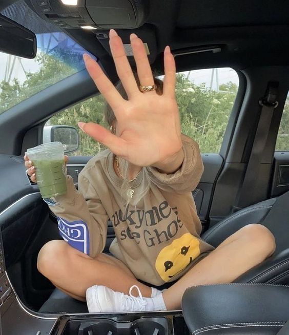 a woman sitting in the back seat of a car with her hand up and holding a drink