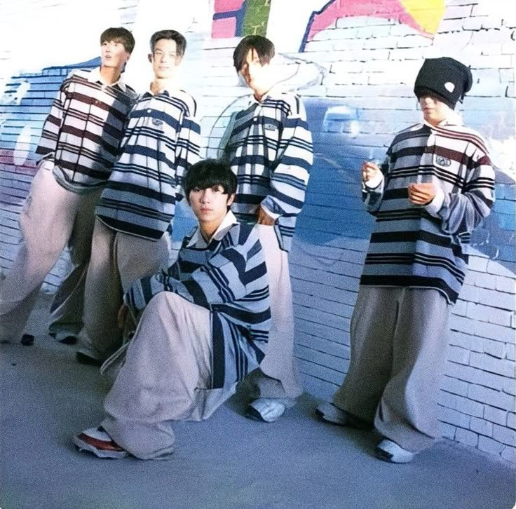 four young men in striped shirts and pants posing for a photo with graffiti on the wall behind them