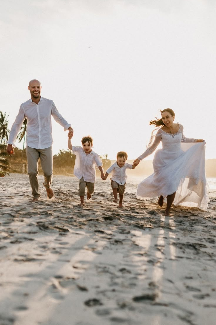 a family running on the beach holding hands and wearing white clothes, all dressed up