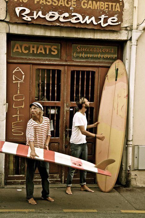 two people standing in front of a building with surfboards leaning against the door,