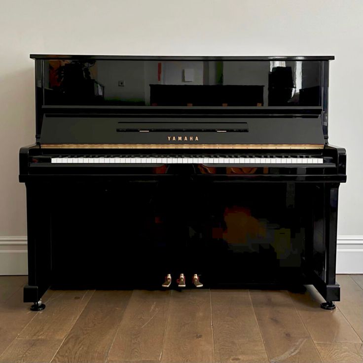 a black piano sitting on top of a hard wood floor next to a white wall