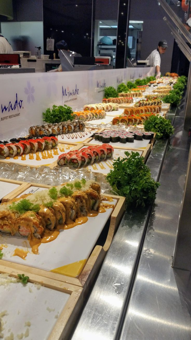 an assortment of sushi on display in a restaurant or buffet line with people working behind the counter