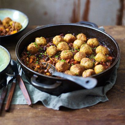 a pan filled with meatballs and vegetables on top of a wooden table next to other dishes