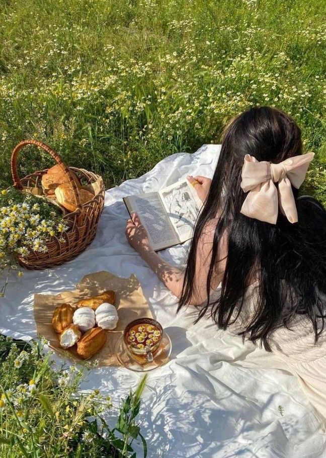 a woman sitting on top of a field next to a basket filled with pastries