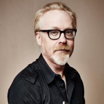 a man wearing glasses and a black shirt is posing for the camera with his arms crossed