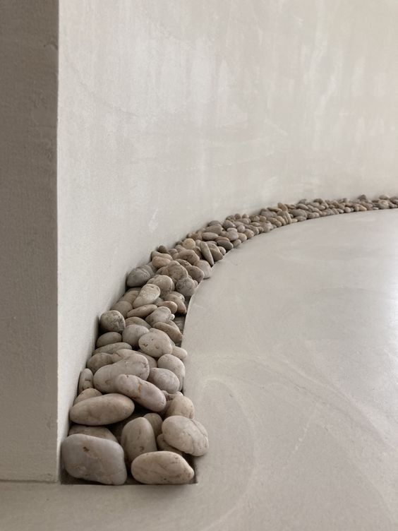 a long line of rocks on the side of a white wall next to a vase