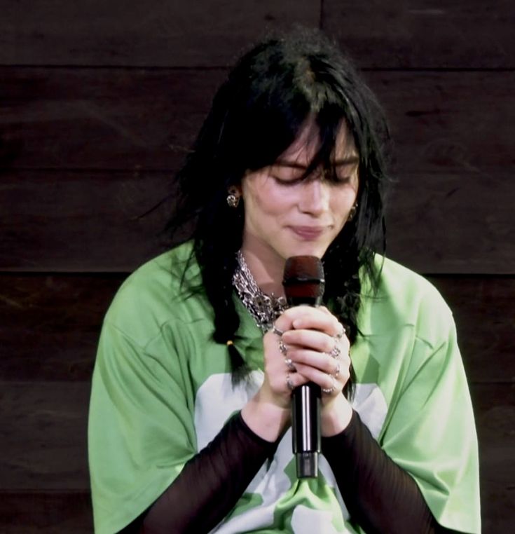 a woman with black hair holding a microphone in front of her face and wearing gloves