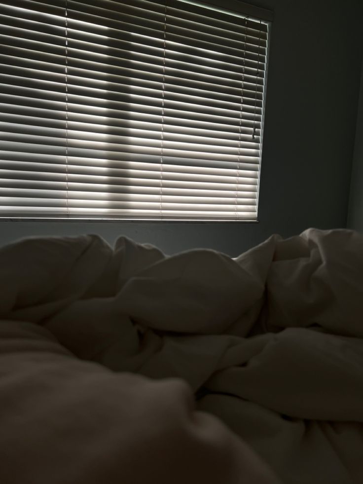 an unmade bed in front of a window with blinds