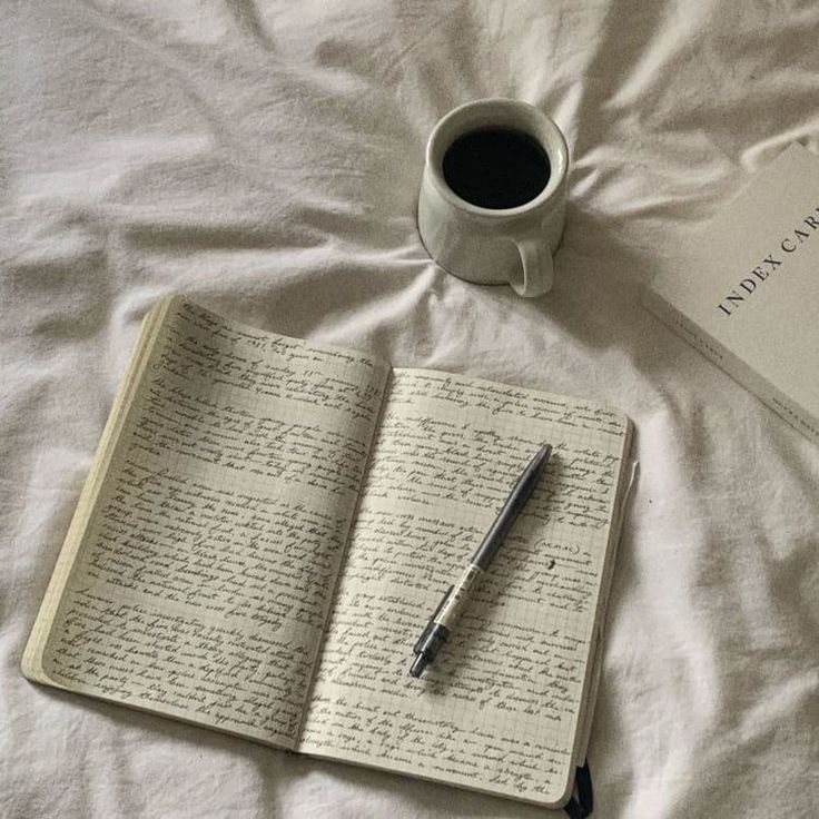 a cup of coffee and an open book on top of a bed with writing in it