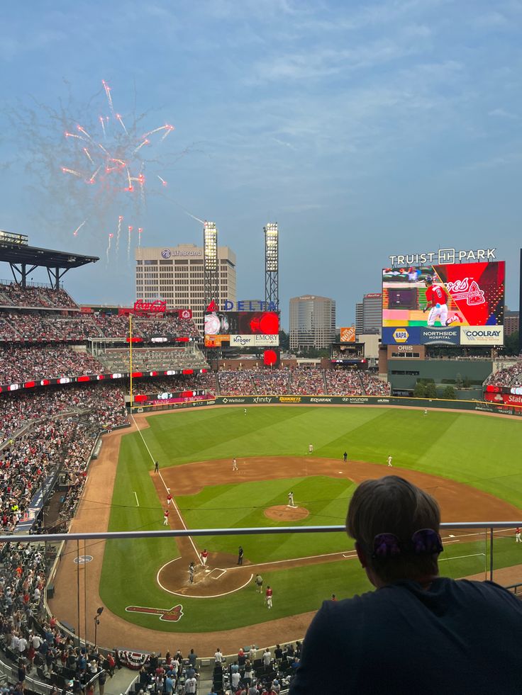 a baseball stadium filled with lots of people watching fireworks go off in the sky above