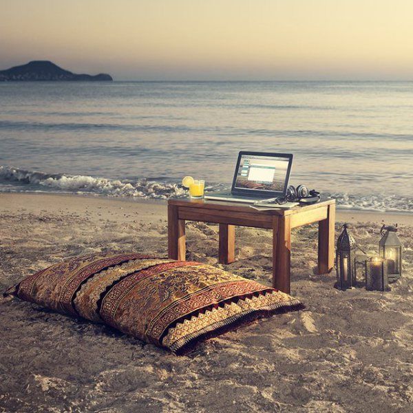 an open laptop computer sitting on top of a wooden table next to the ocean and beach