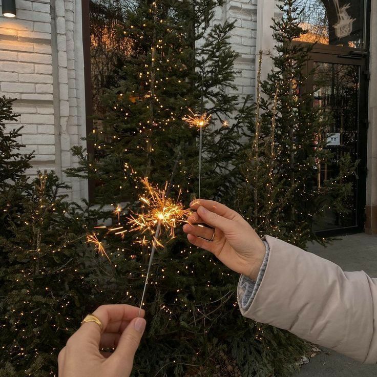 two people are holding sparklers in front of a christmas tree with lights on it