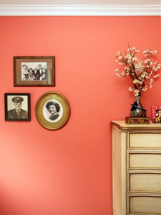 an orange wall with pictures on it and flowers in vases next to the dresser