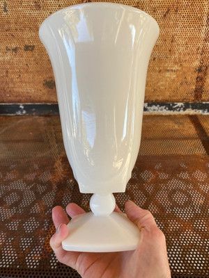 a white vase being held up by someone's hand on top of a table