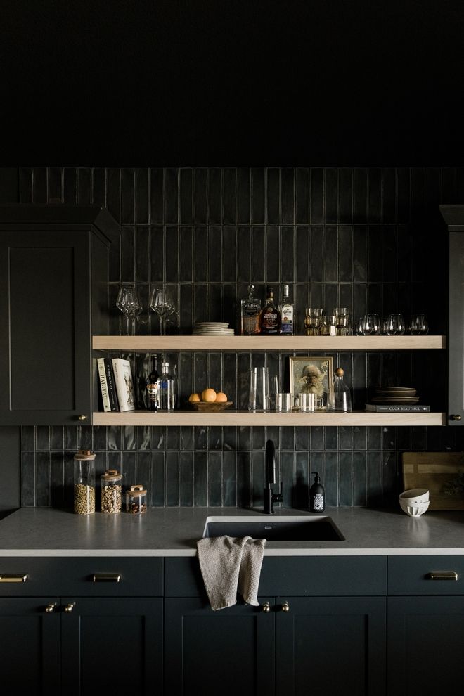 a kitchen with black cabinets and shelves filled with bottles, glasses, and other items