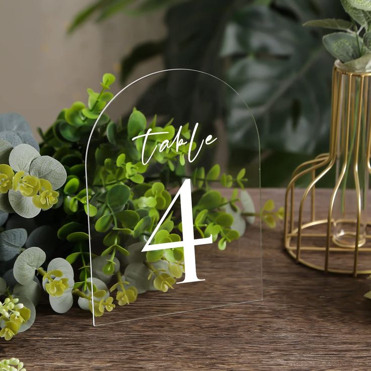 the table numbers are placed on top of each other and surrounded by greenery, including succulents