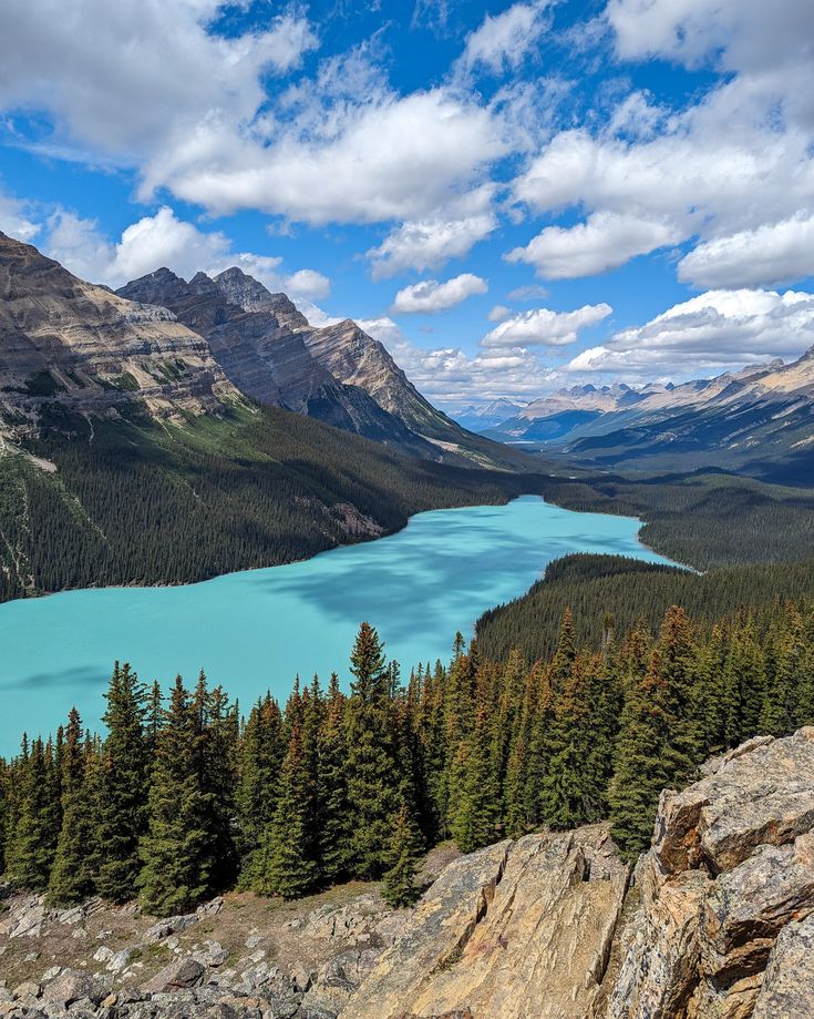 a lake surrounded by mountains and trees under a blue sky with clouds in the background