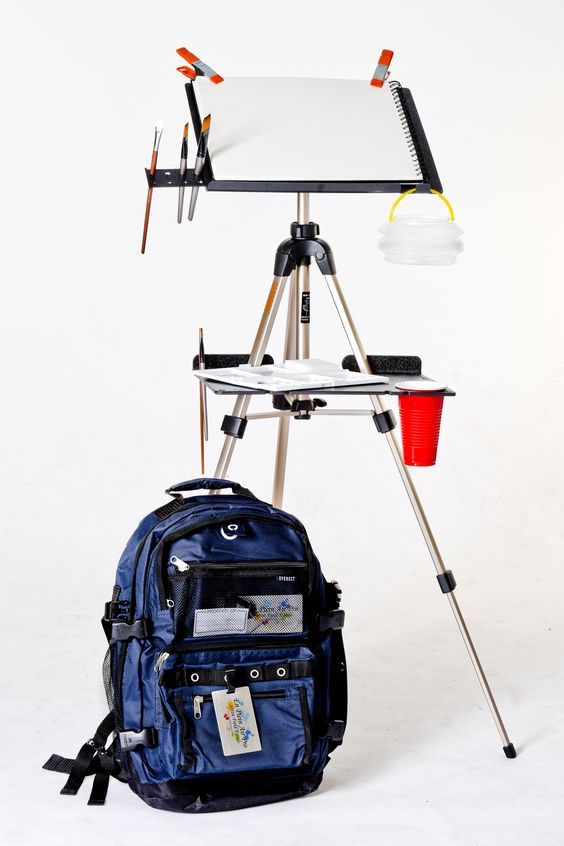 an easel, backpack and camera on a tripod with a white board in the background