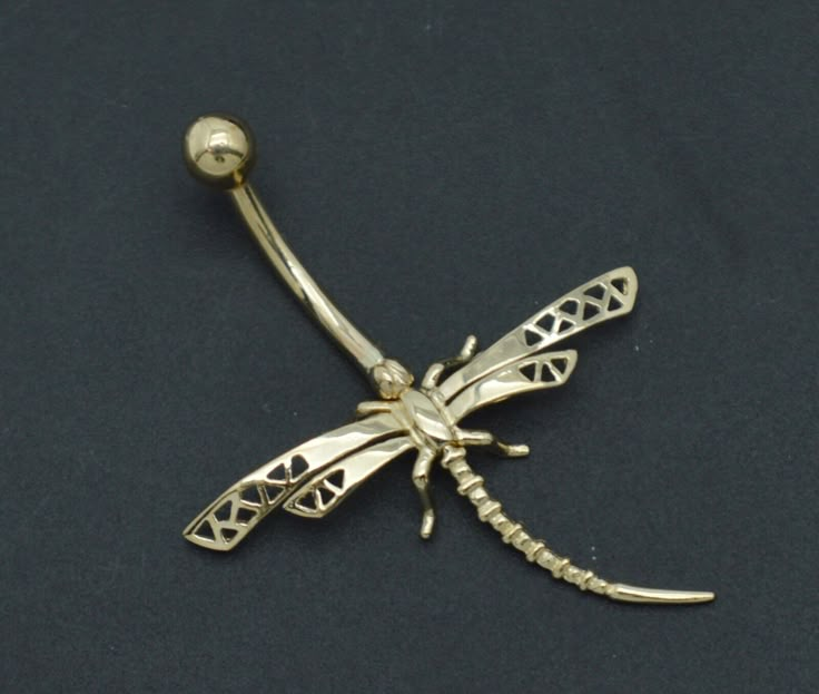 a gold colored dragonfly belly ring on a black surface with a ball in the middle