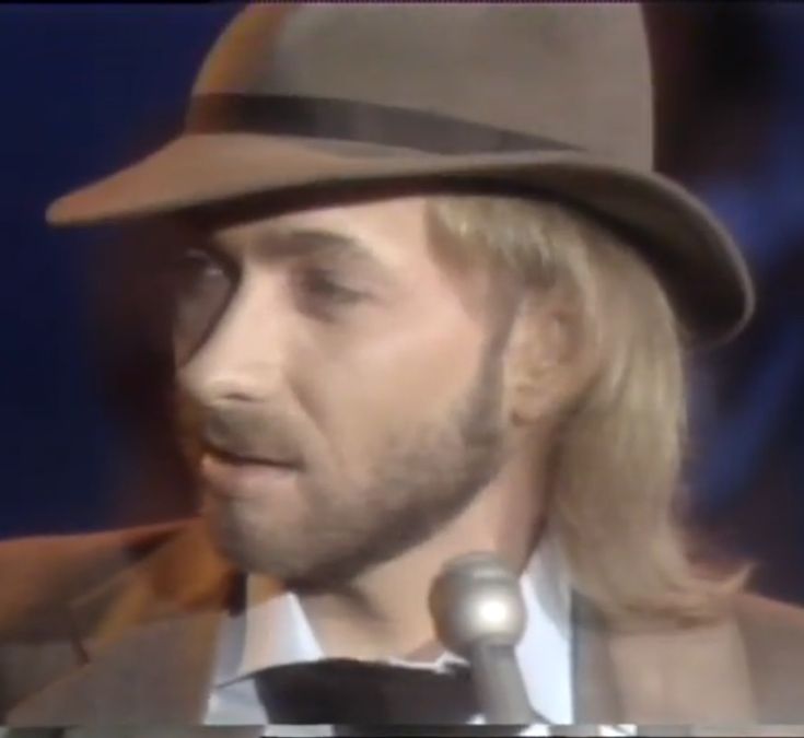 a man with long hair wearing a fedora and a suit in front of a microphone