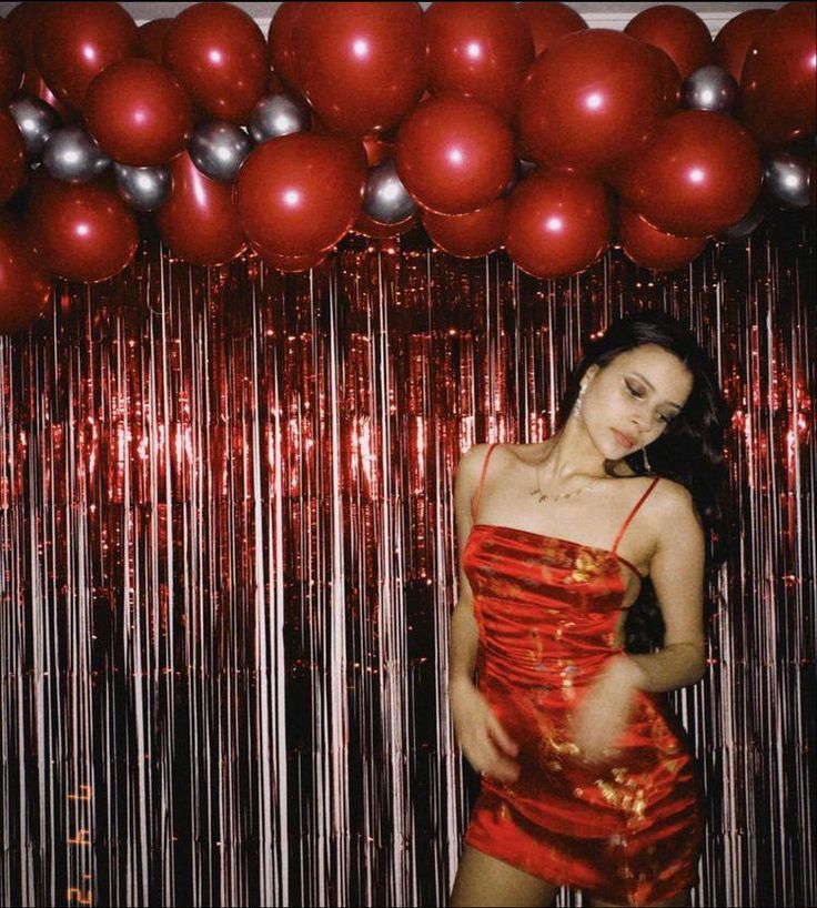 a woman standing in front of red and silver balloons with her hands on her hips