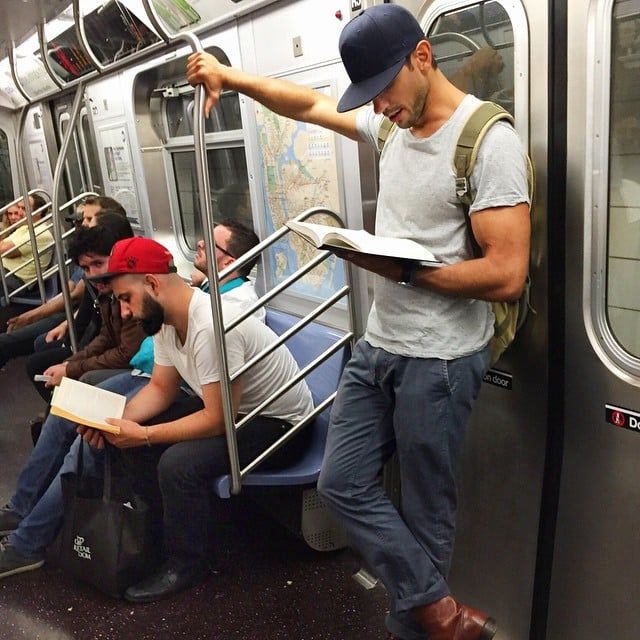 a man reading a book while riding on a subway train with other people sitting in the seats