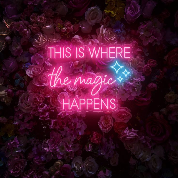 a neon sign that says, this is where the magic happens in front of flowers