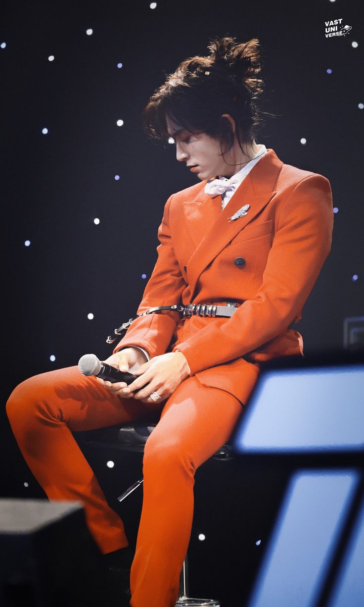 a man in an orange suit is sitting on a chair and looking at his cell phone