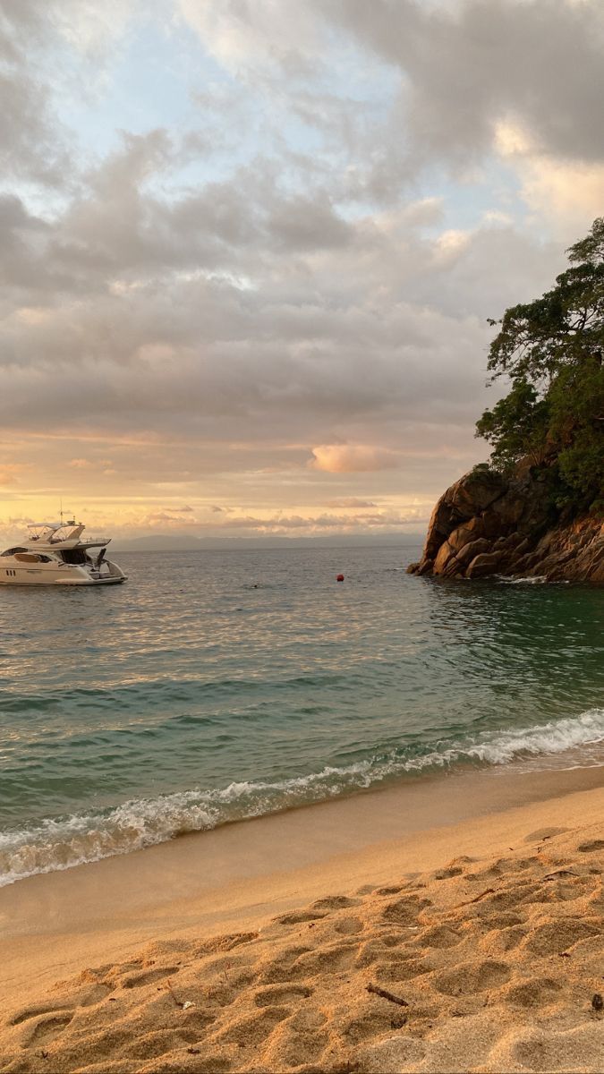 a boat is out on the water near a sandy beach with footprints in the sand