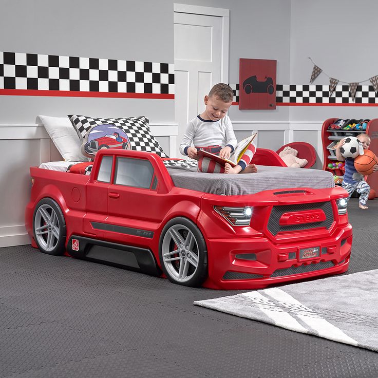 a young boy sitting in his red truck bed reading a book while another child stands next to him