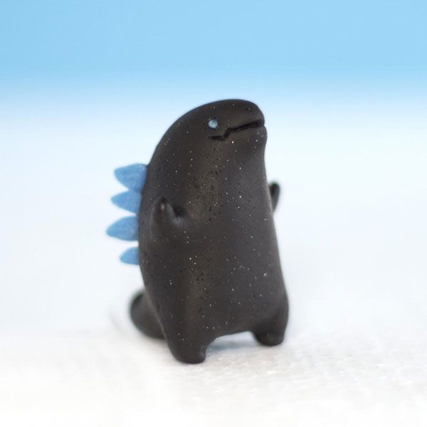 a small black toy with blue wings on it's head and eyes, sitting on a white surface