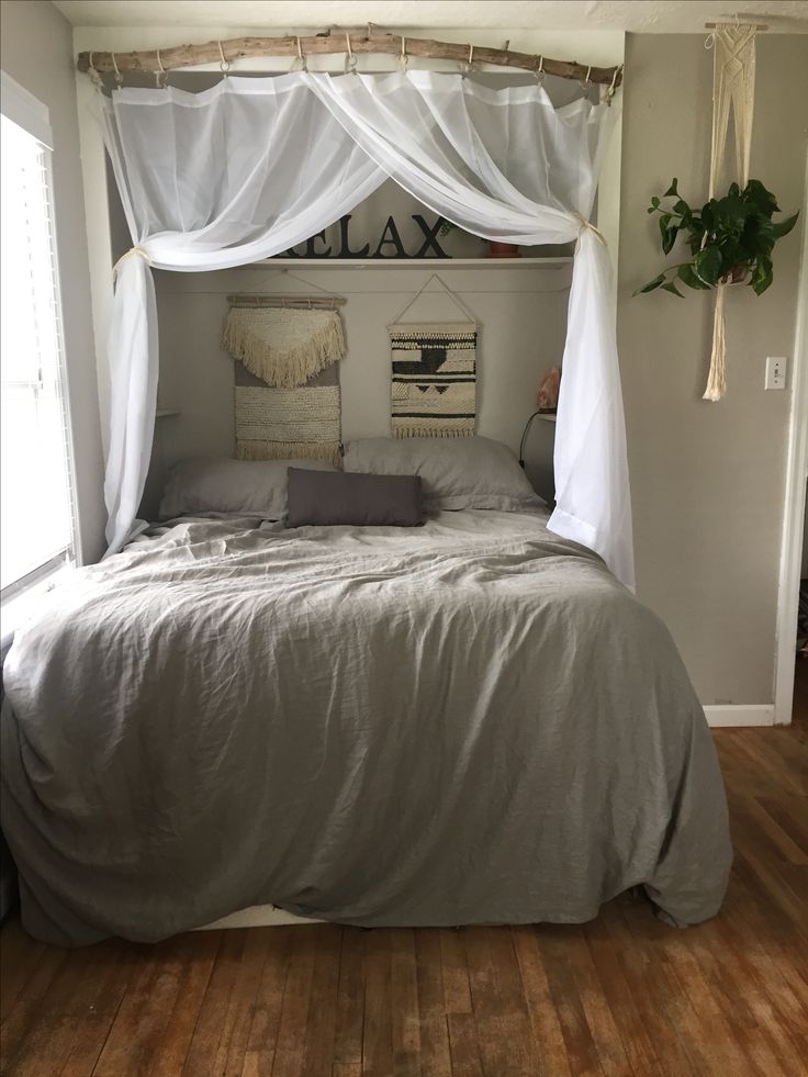 a bed with white drapes on top of it and a wooden floor in front of the bed