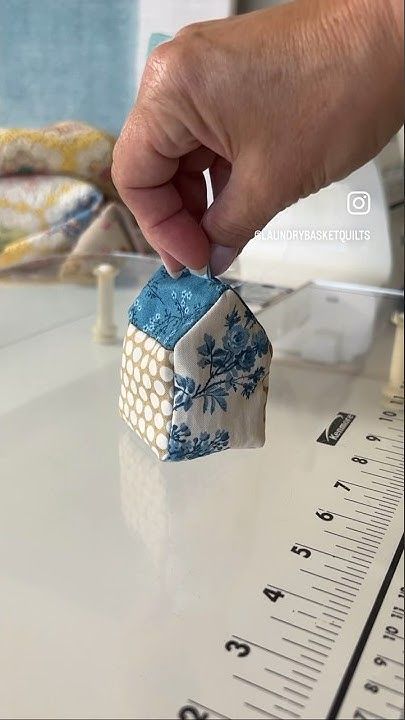 a hand is holding a small blue and white house ornament on top of a ruler