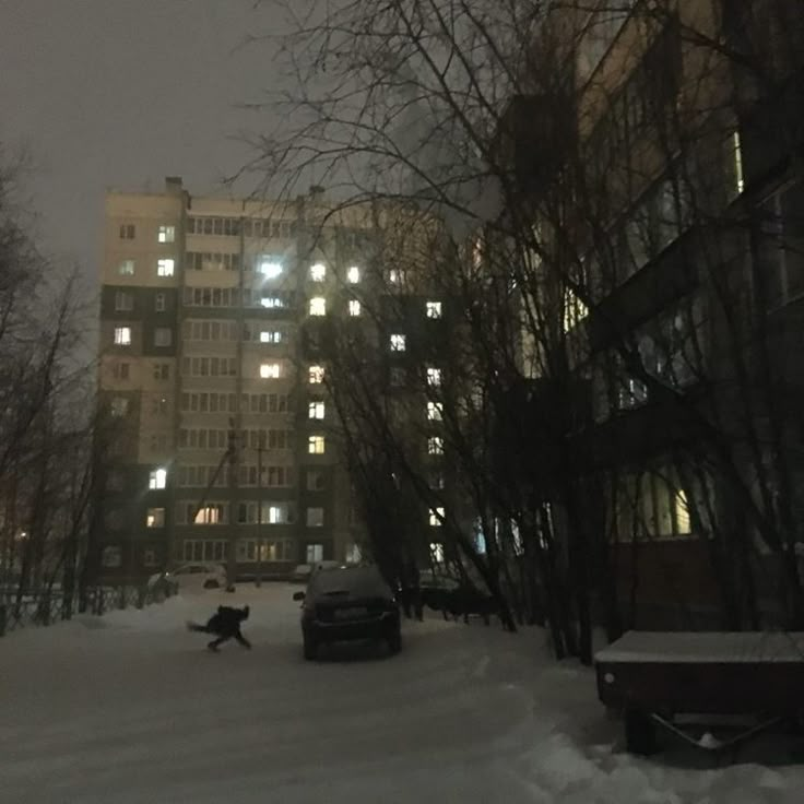 a person riding a snowboard down a snow covered street in front of tall buildings