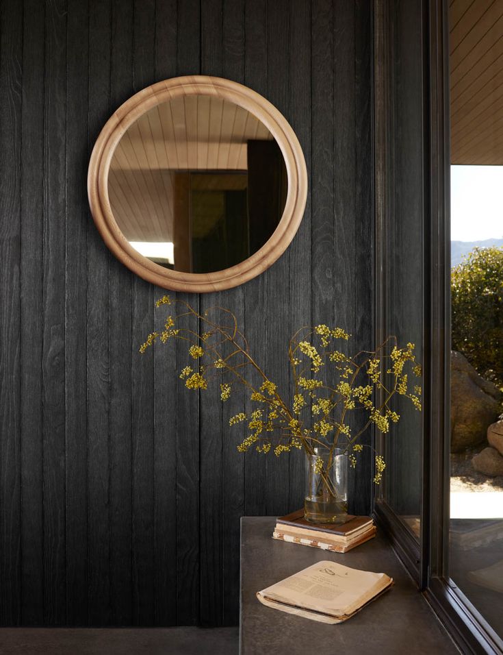 a vase filled with flowers sitting next to a mirror on top of a wooden wall