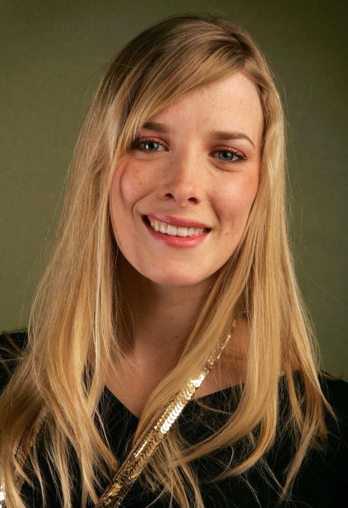 a woman with long blonde hair smiles at the camera while wearing a black shirt and gold necklace