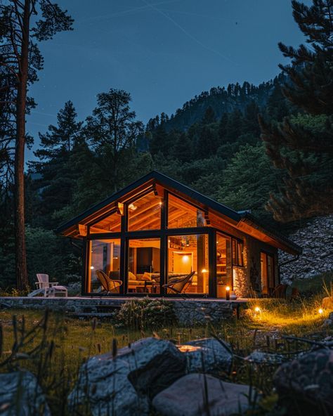 a small cabin is lit up at night in the woods with rocks and trees surrounding it