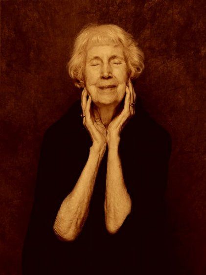 an older woman with her hands on her face, posing for a photo in front of a brown background