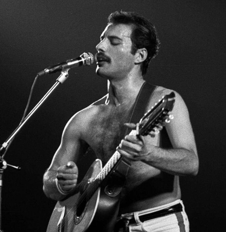 a shirtless man singing into a microphone while holding a guitar in his right hand