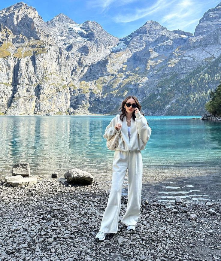 a woman standing on top of a rocky beach next to a body of water with mountains in the background