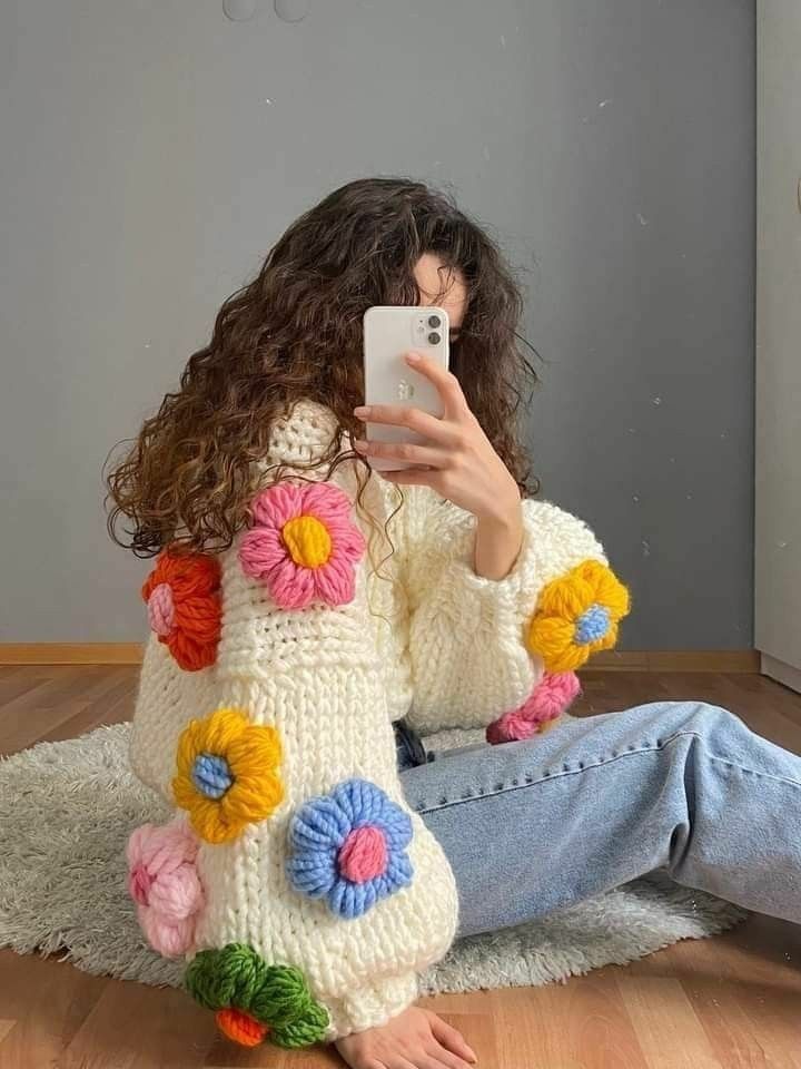 a woman is sitting on the floor taking a selfie with her cell phone while wearing a colorful sweater