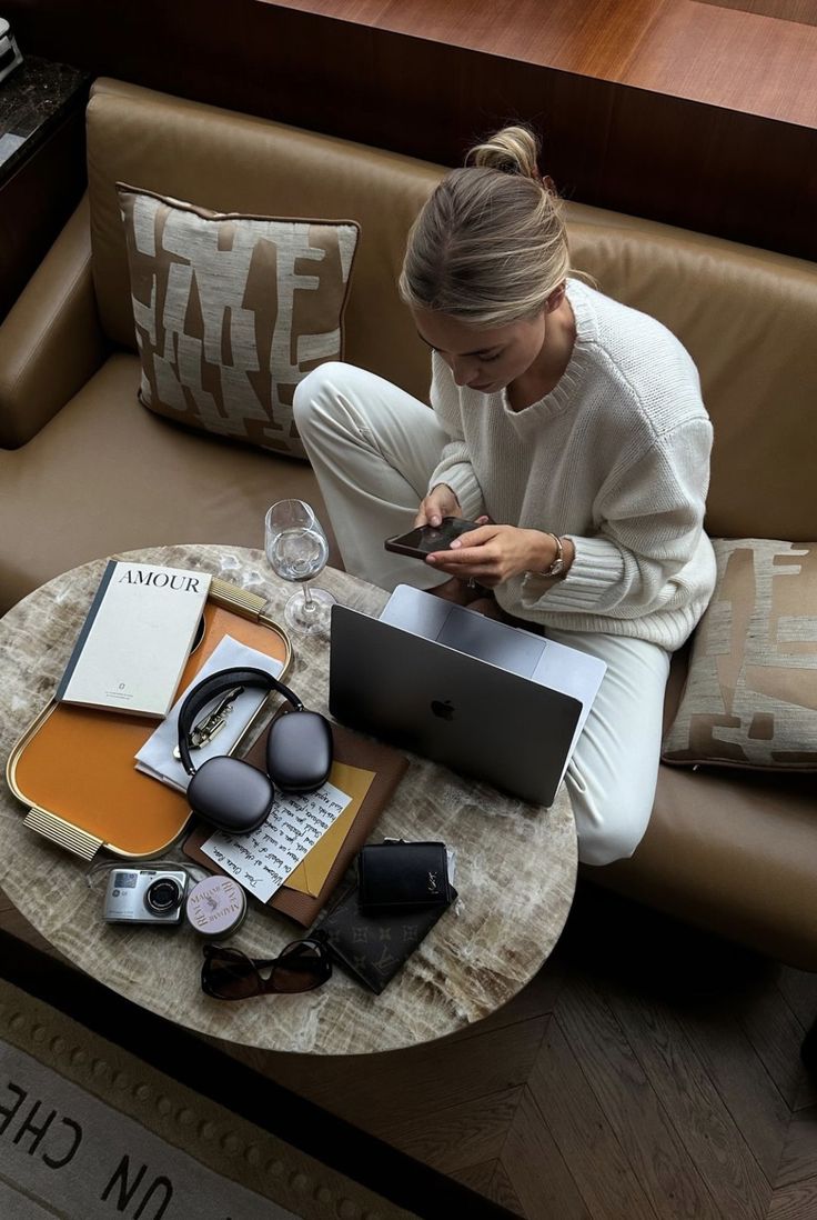 a woman sitting on a couch looking at her cell phone and laptop computer with headphones