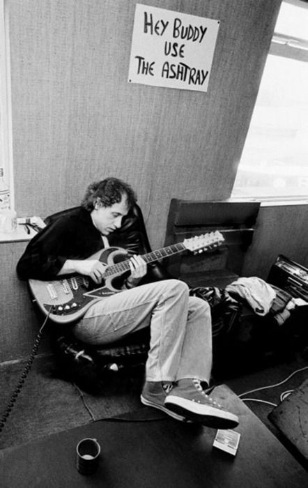 a man sitting in a chair with a guitar on his lap and a sign that says hey buddy use the astrayry