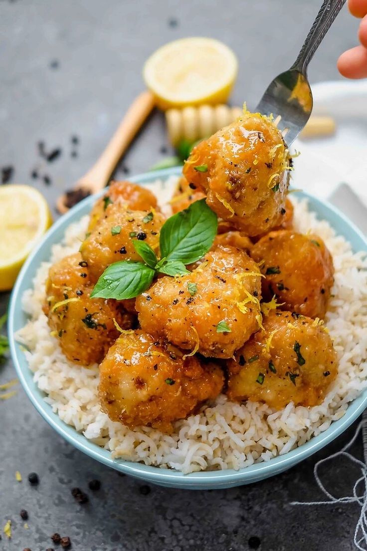 a bowl filled with rice and meat covered in sauce next to lemon wedges on the side